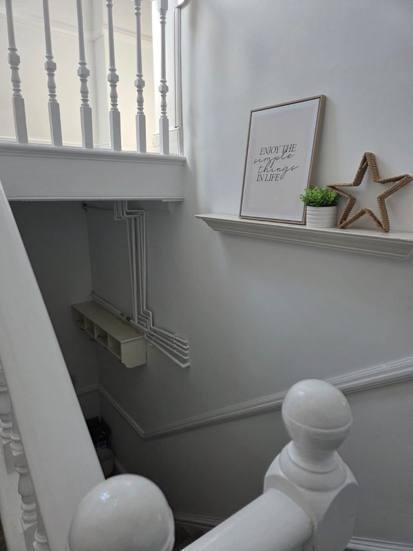 Stairwell with white railings, shelf with framed print and decorative star, potted plant