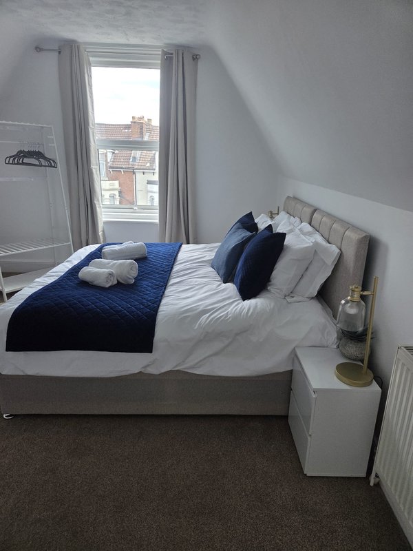 Bright bedroom with double bed, navy bedding, pillows, and window overlooking street