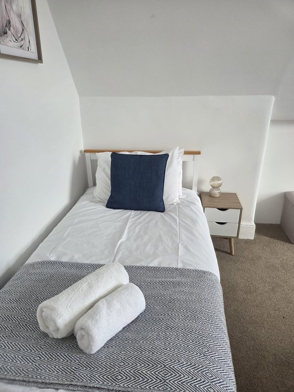 Modern bedroom with single bed, white headboard, navy cushion and rolled white towels