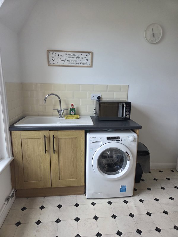 Utility room with sink, wooden cabinet, washing machine, and black and white tile floor