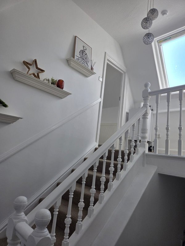 Bright staircase with white walls, wooden railings, floating shelves with decorative items