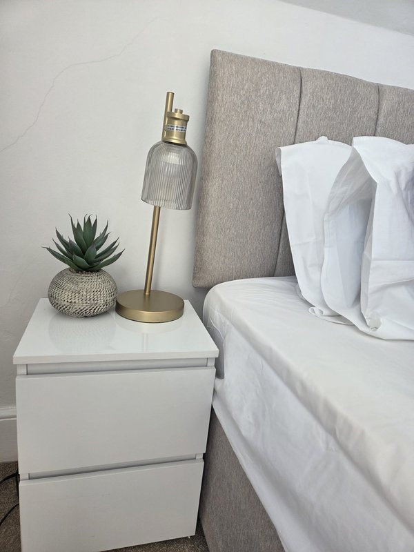 Modern bedroom with white nightstand, grey upholstered headboard, potted succulent and brass lamp