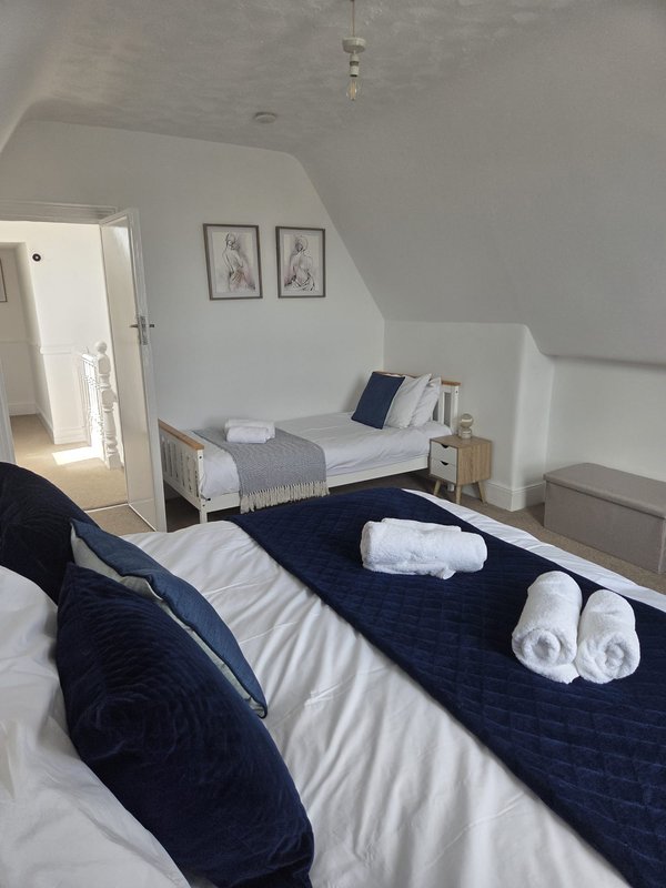Bright attic bedroom with two beds, white walls, wooden furniture and framed wall art