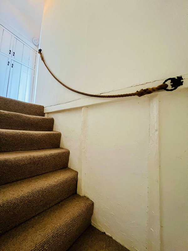 Staircase with brown carpet treads and rope handrail in a plain white hallway