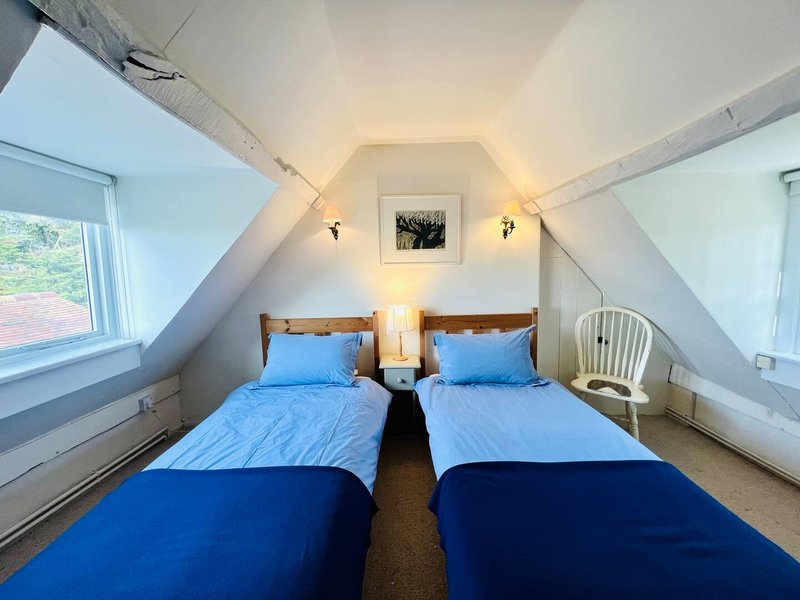 Attic bedroom with two single beds with blue bedding, skylights, and wall sconces