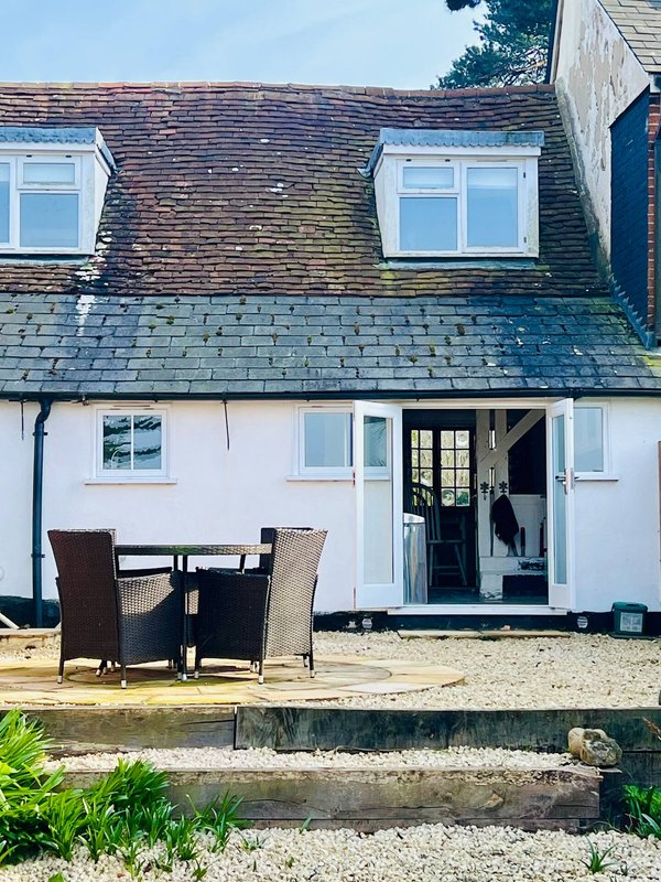White cottage exterior with slate roof, patio seating area and glass doors