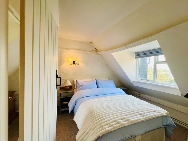 Attic bedroom with blue and white bedding, skylight window, wall sconce and wooden wardrobe