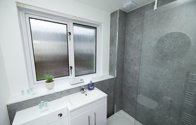 Modern bathroom with white vanity, grey tile walls, frosted window and shower enclosure
