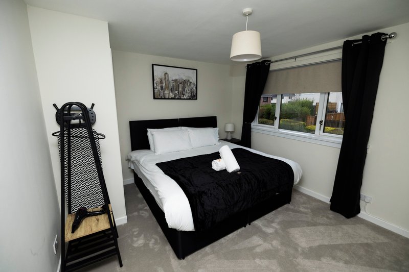 Modern bedroom with black and white bed, pendant light, black curtains and garden view