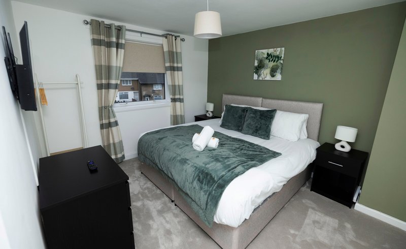 Modern bedroom with double bed, green accent wall, kitchenette, and pendant lighting