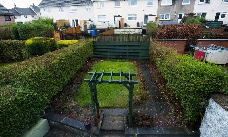 Rear garden with green hedges, pergola structure, and neighboring residential properties visible