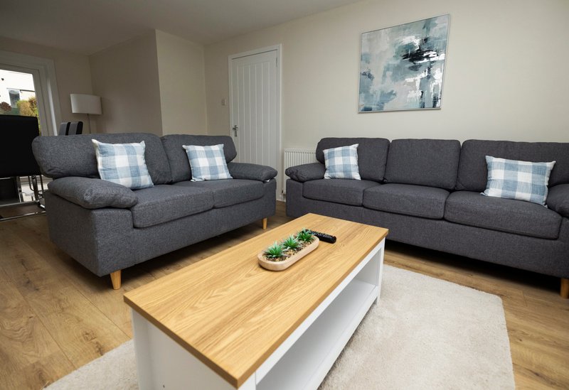 Spacious living room with two grey sofas, wooden coffee table, white door and abstract wall art
