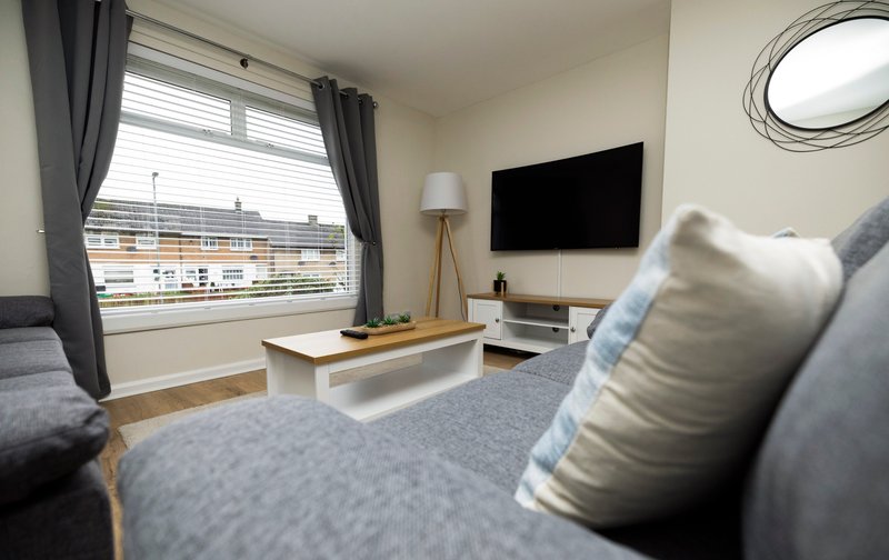 Modern living room with grey sofa, wall-mounted TV, wooden coffee table and large window