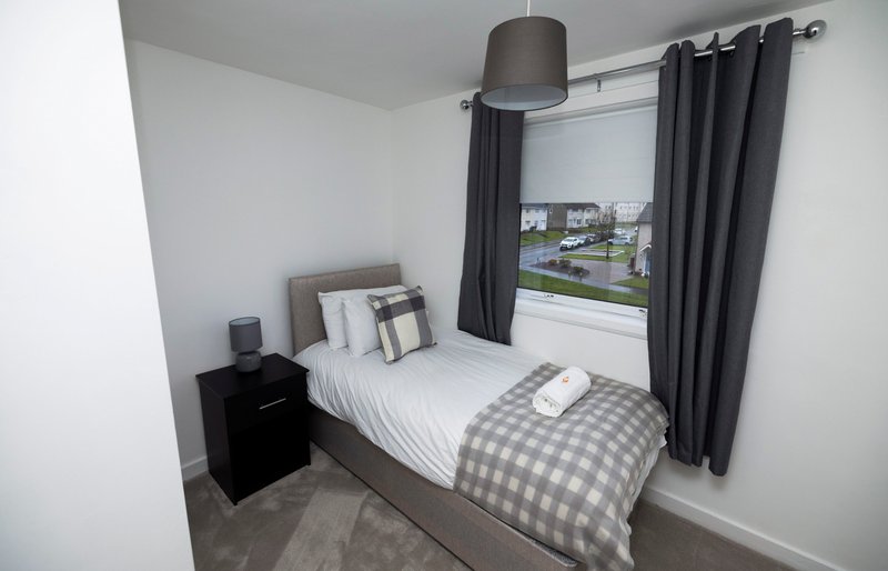 Bedroom with single bed, gray checkered bedding, black nightstand and pendant lamp