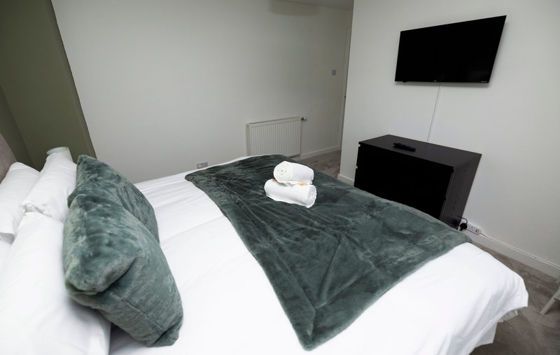Bedroom with double bed, green velvet throw, white pillows, wall-mounted TV and storage unit