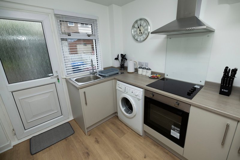 Modern kitchen with white cabinets, integrated appliances, wooden countertops and door to garden