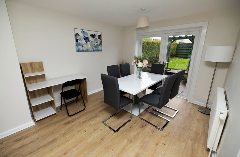 Modern dining room with white table, black chairs, wooden shelving unit and garden view