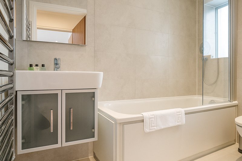 Modern bathroom with white sink vanity, bathtub, shower enclosure and heated towel rail