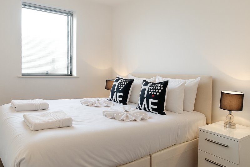 Modern bedroom with white bed, decorative pillows, bedside table and lamp