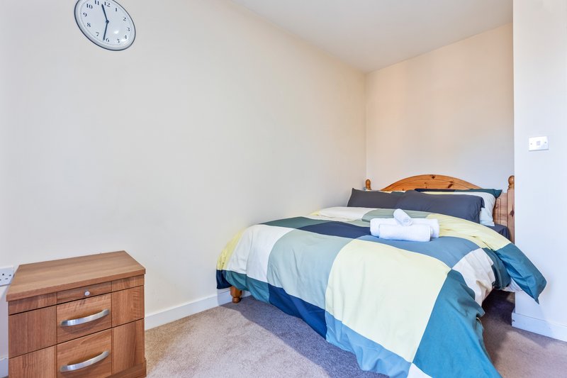 Bedroom with wooden bed frame, blue and white bedding, wooden nightstand, and wall clock