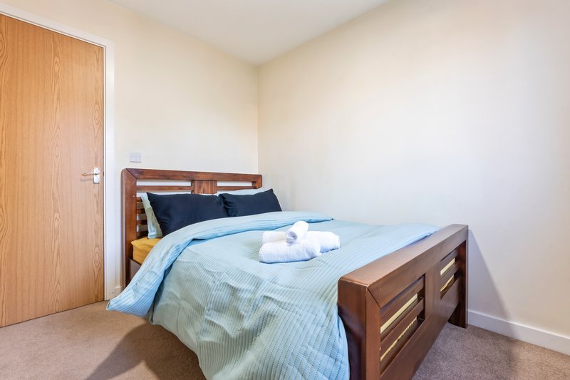 Bedroom with wooden bed frame, blue bedding, folded towels, and wooden door
