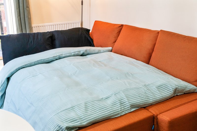 Bedroom with orange upholstered bed, blue and white striped bedding, dark headboard and window with curtains