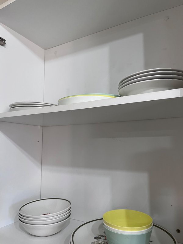 Kitchen cupboard shelf with stacked white bowls and yellow-lidded storage containers