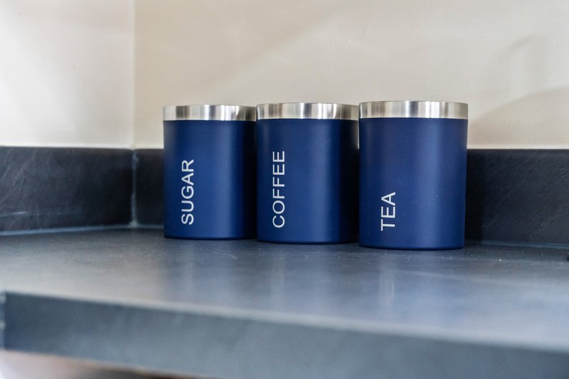 Three blue storage containers labeled sugar, coffee and tea on kitchen counter