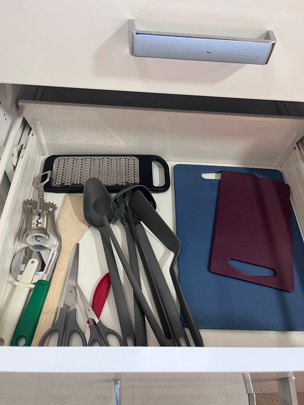 Kitchen drawer open showing cooking utensils, grater, and folded kitchen towels