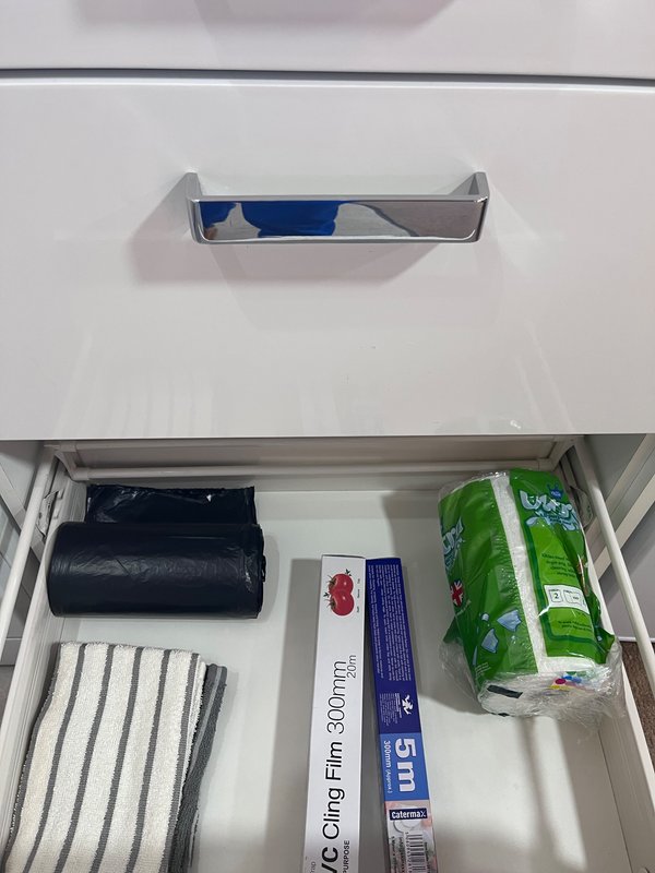 Kitchen drawer containing paper towels, plastic bags, and household supplies