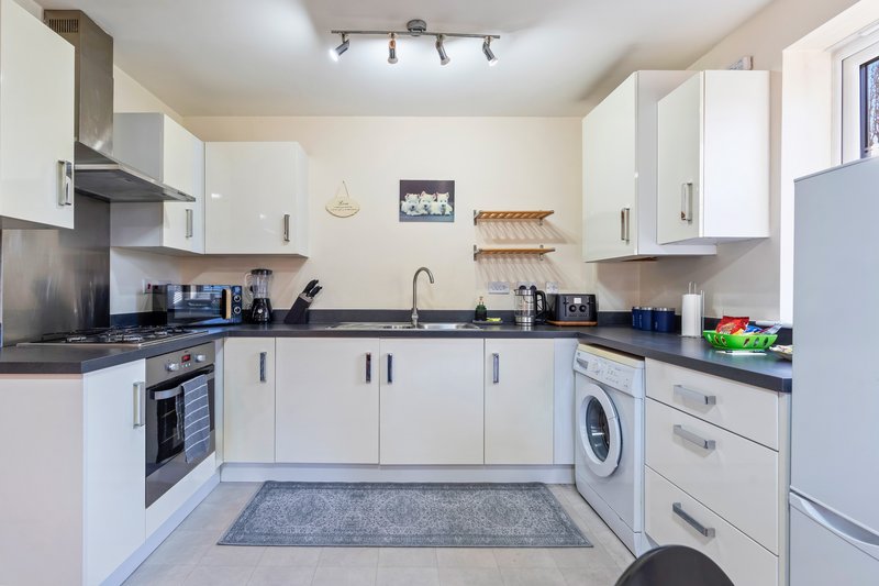 Modern kitchen with white cabinetry, black countertops, integrated appliances and washing machine