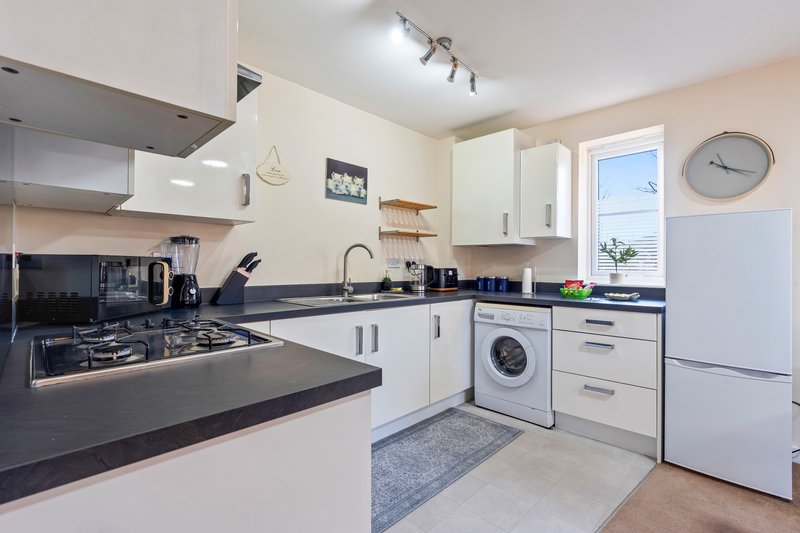 Modern kitchen with white cabinets, black countertops, gas hob, washing machine and refrigerator