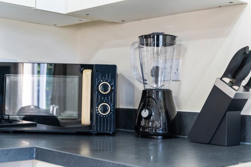 Modern kitchen counter with black appliances including microwave, blender and knife block