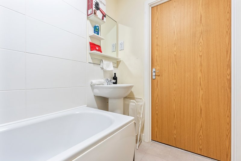 Bathroom with white bathtub, pedestal sink, wall-mounted shelving and wooden door