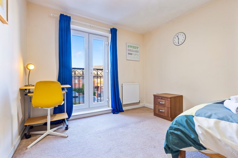 Bedroom with double bed, yellow desk chair, blue curtains and balcony doors