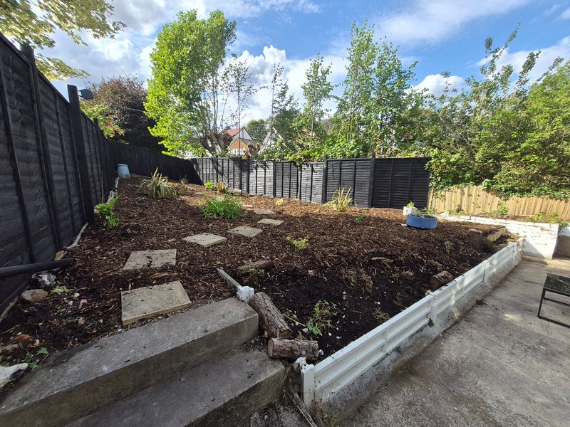 Garden area with raised beds, black fencing, patio, and mature trees