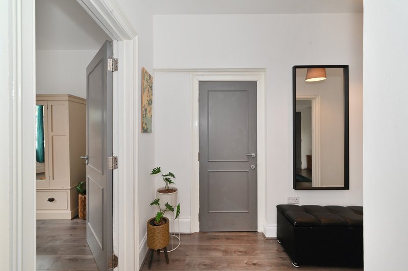 Hallway with gray door, potted plants, mirror, and black seating area