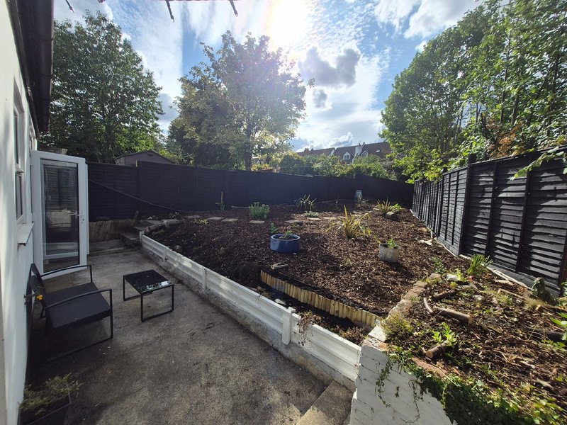 Backyard garden with raised beds, black fencing, patio area and mature trees