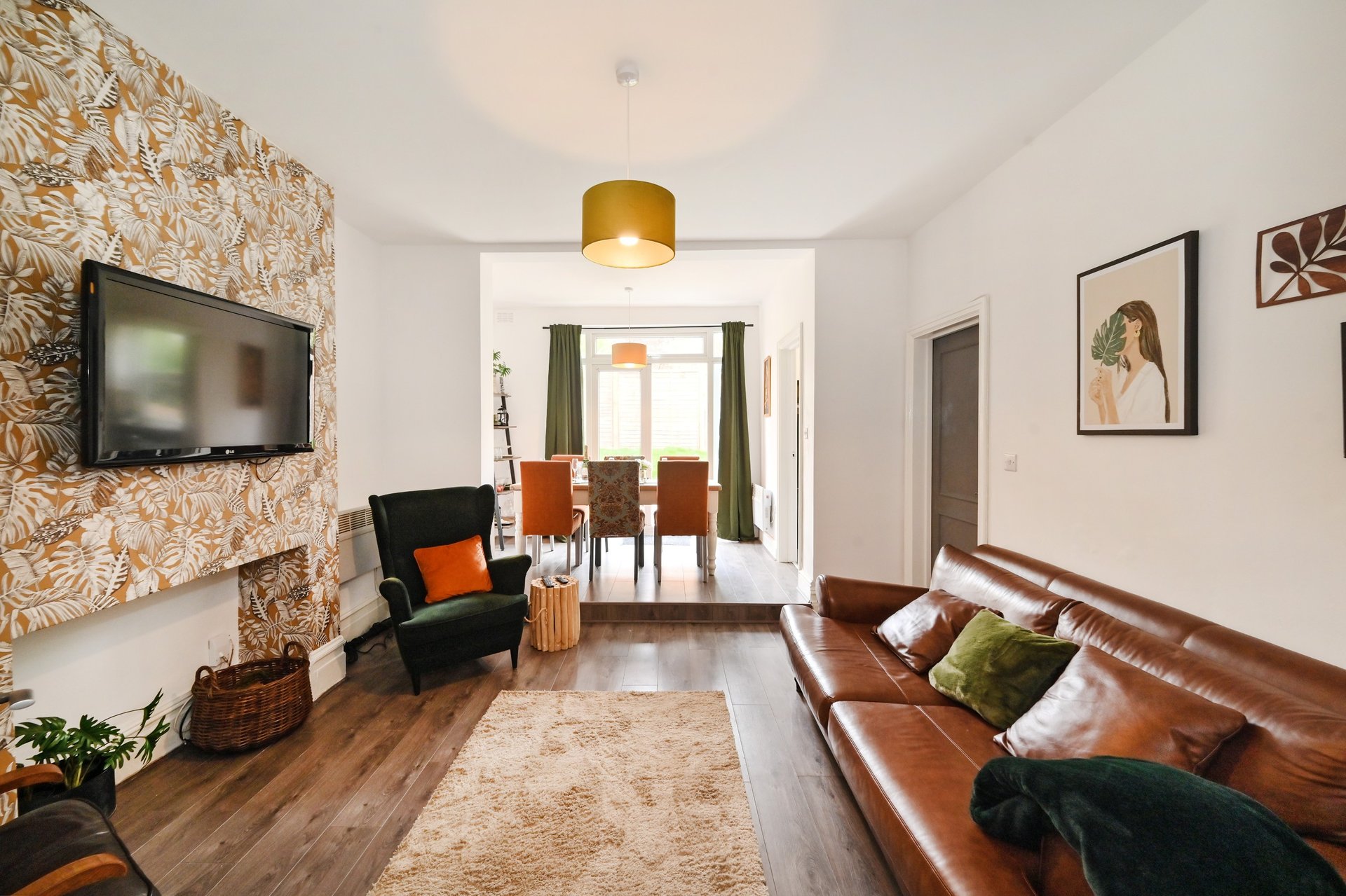 Modern living room with leather sofa, armchair, wall-mounted TV, and wooden flooring
