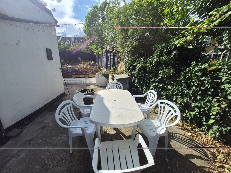 Outdoor patio area with white plastic furniture, table, and ivy-covered fence