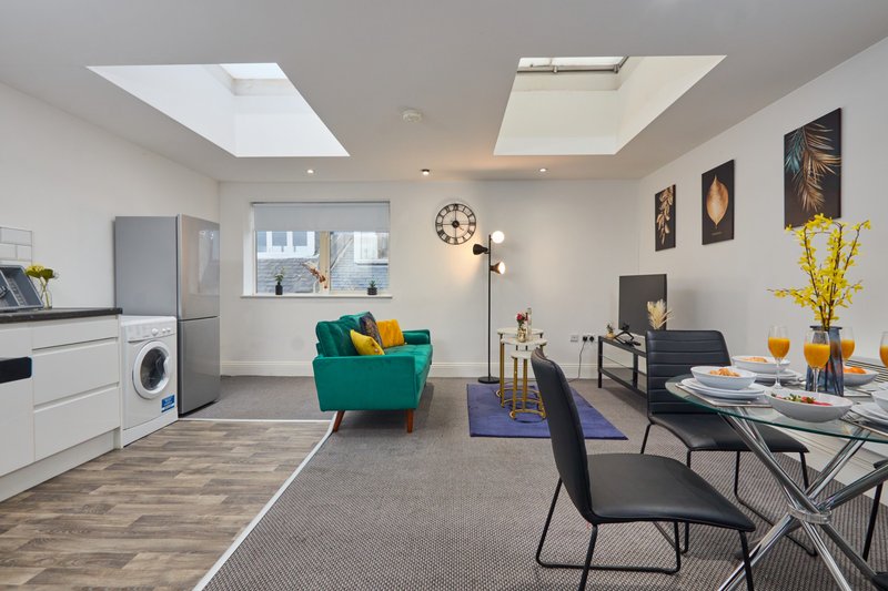 Open-plan living space with kitchen, teal armchair, dining table, and skylight windows