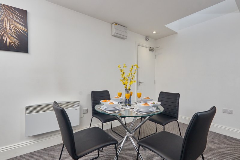 Dining area with round glass table, four black chairs, yellow flowers and place settings