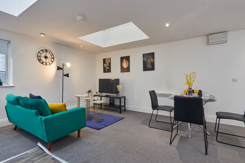 Modern open-plan living area with turquoise sofa, dining table, desk, and skylight