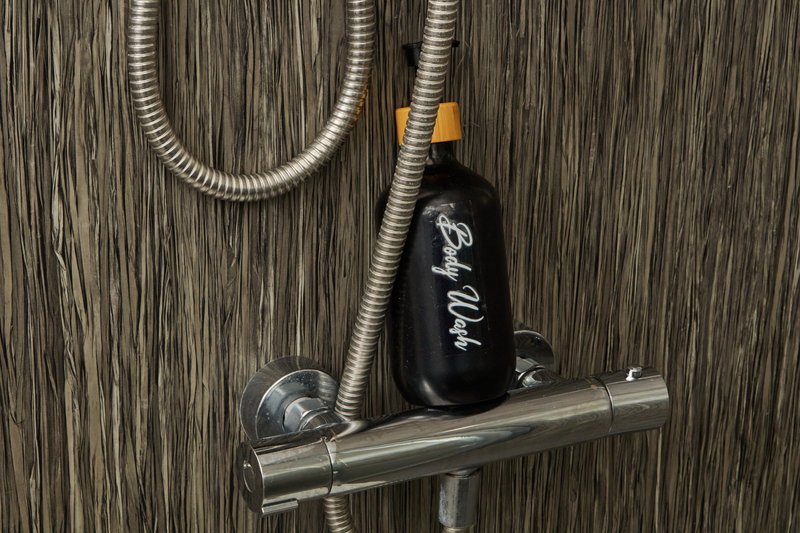 Bathroom shower head with metal fixtures and black soap bottle on shelf