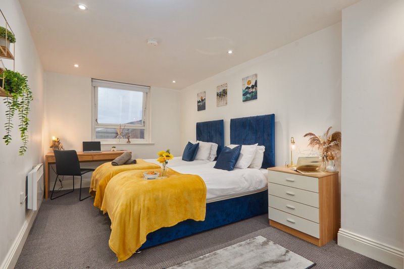 Modern bedroom with double bed, yellow throw, blue headboard, wooden furniture and desk area