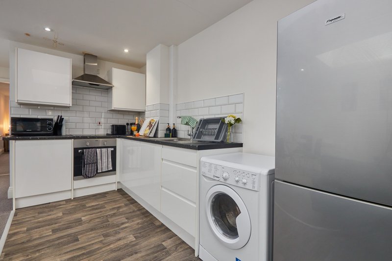 Modern kitchen with white cabinets, stainless steel appliances, washing machine and wooden flooring