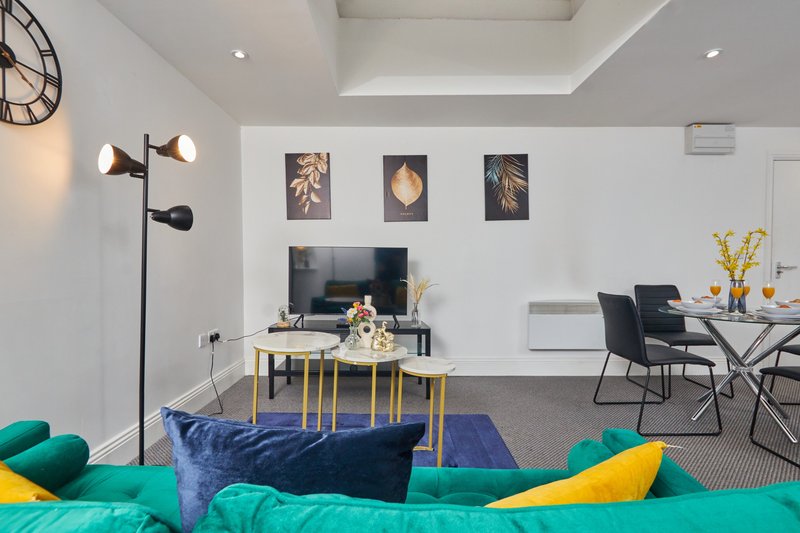 Modern open-plan living room with teal sofa, TV on wall-mounted stand, dining area, and decorative wall art