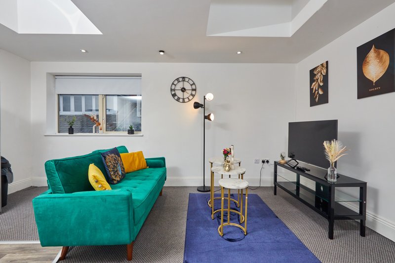 Modern living room with turquoise sofa, blue rug, black TV stand, and skylight windows