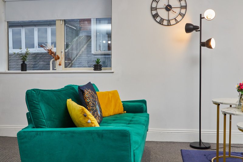 Modern living room with teal armchair, colorful cushions, floor lamp and wall clock