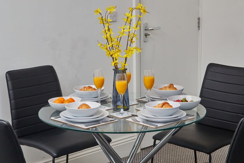 Dining table set for four with place settings, orange juice glasses, and yellow flower arrangement